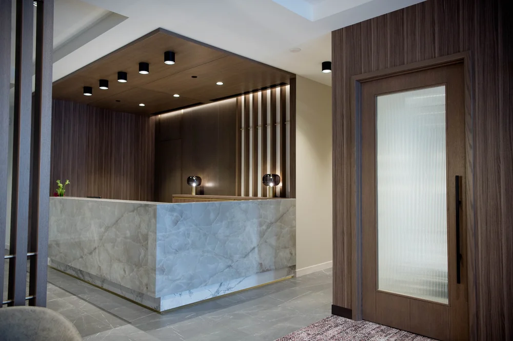 Modern reception area with a marble front desk, wooden paneling, and contemporary light fixtures.