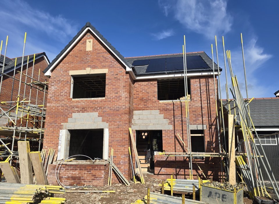 Newly constructed brick house with scaffolding and construction materials visible around the structure.