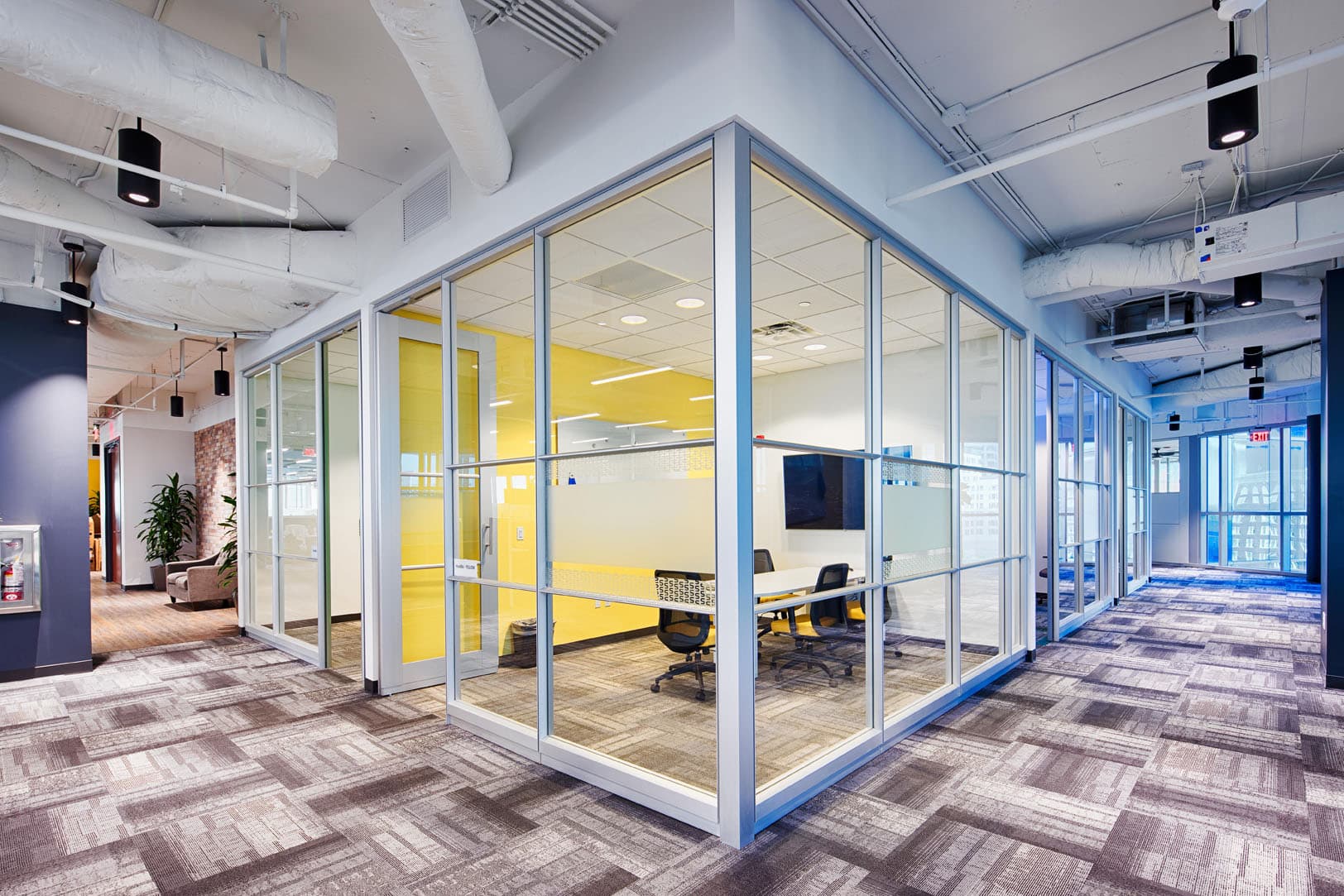 Modern office space featuring glass-walled meeting rooms with yellow accents and a contemporary design.