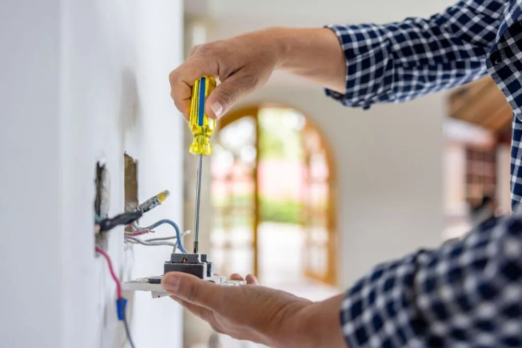 Person using a screwdriver to work on an electrical outlet, with wires visible in the background.